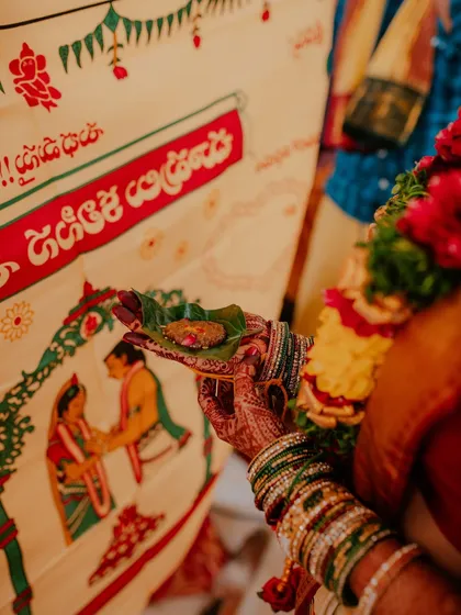 A close-up of the bride's hand, adorned with henna and bangles, holding a betel leaf during a wedding ritual.