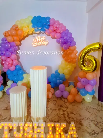 A bright and cheerful rainbow-themed 6th birthday party. The decor includes a circular balloon arch with rainbow colors, a neon sign, and a large gold foil number '6' balloon.