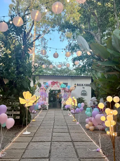 The magic should start the moment your guests arrive. For this enchanted forest party, I designed a grand entrance path with glowing floral lights, string lanterns, and balloon clusters to guide everyone into a fairytale world, transforming this beautiful backyard space.