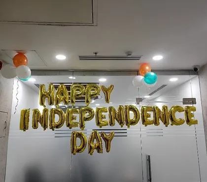 "Happy Independence Day" spelled out in gold foil balloons in an office setting.