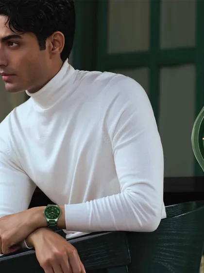 A clean and modern product styling shot for the Titan Edge ceramic watch collection. The look is minimalist, with a simple white turtleneck and neutral trousers, ensuring the deep green of the watch stands out as the hero of the image.