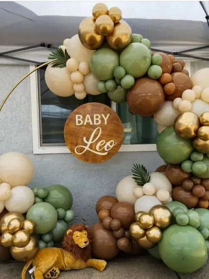 A 'Baby Leo' jungle-themed baby shower. This setup features a circular frame decorated with an organic balloon garland in safari-inspired colors like olive green, brown, and gold, with a cute lion plush to guard the scene.