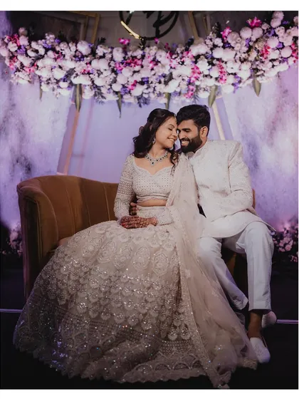 Adarsh and Premika share a quiet moment together during their reception, seated under a beautiful floral arrangement.