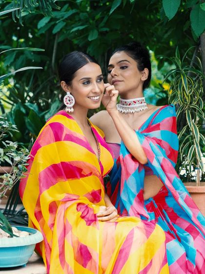 Two models in vibrant, colorful sarees share a moment in a lush garden setting. This shot is perfect for showcasing a collection's variety and creating a joyful, friendly brand image.