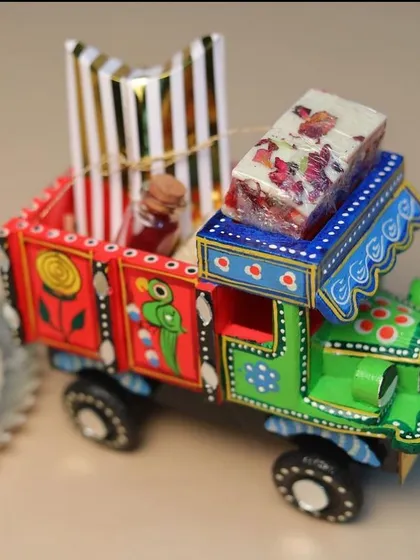 Our 'Desi Gaddi' (Indian Truck) hamper is a unique and quirky Rakhi gift. This hand-painted wooden truck is filled with roli, chawal, a rakhi, and a sweet treat.