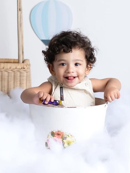 This adorable little boy is enjoying his ride in a bucket, surrounded by clouds. The hot air balloon theme is a favorite for creating dreamy and imaginative portraits.