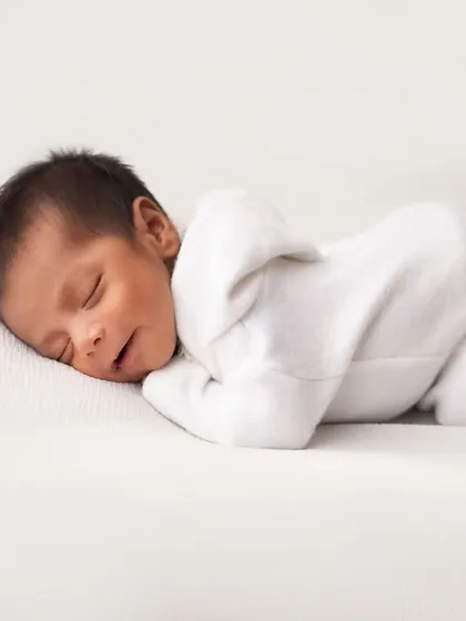 A pure and simple portrait on a clean white background. This pose, with the baby in a simple white outfit, focuses entirely on their perfect newborn form.