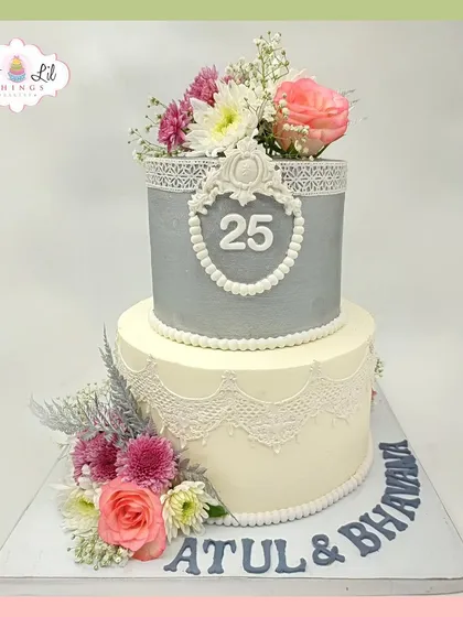 A grand 25th anniversary cake for Atul and Bhavna, featuring silver and white tiers with intricate lace details and fresh flowers.