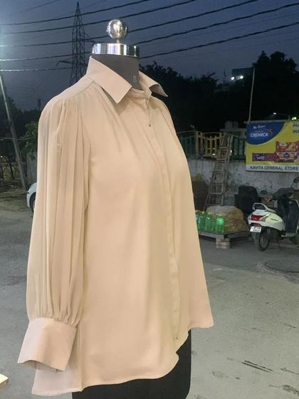 Another view of the custom-stitched beige shirt, showing the detail of the pleated sleeves and the clean, classic collar.