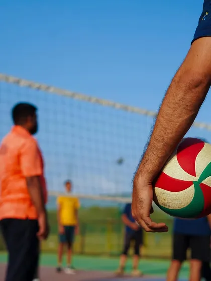 A hand holding a Molten volleyball, with the court and net in the background. The ball is the heart of the game, and we use only the best.