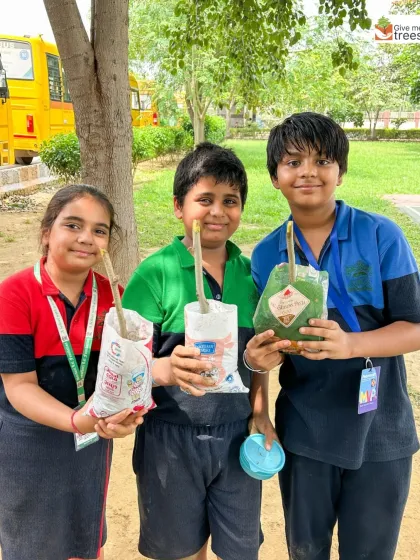 Proud students hold up saplings they've potted in reused milk packets. This teaches them a valuable lesson in resourcefulness and reducing waste.