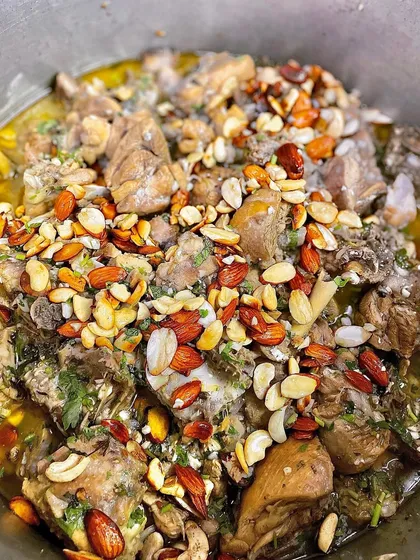A large pot of Chicken Mandi being prepared, with tender chicken pieces topped with a generous amount of fried nuts for a crunchy texture.
