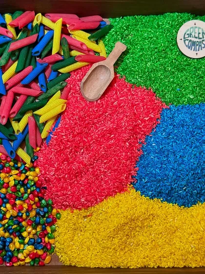 A close-up of a vibrant sensory bin, filled with colorful rice, pasta, and corn. These kits are designed to stimulate the senses and are a great example of the educational products you can find at my events.