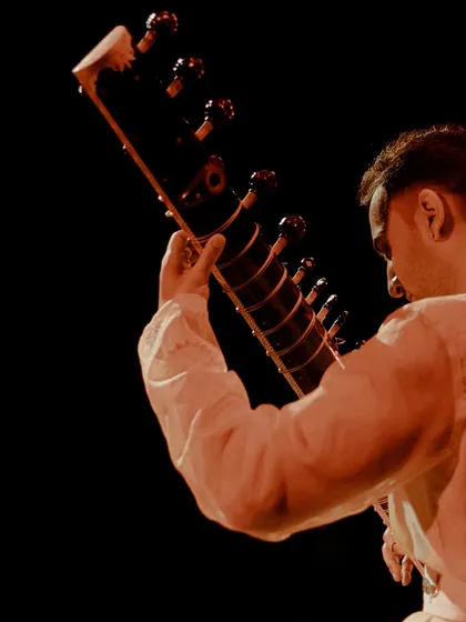 A shot from behind, focusing on the sitar against the dark, vast stage. It highlights the instrument as the central voice of the evening's meditative journey.