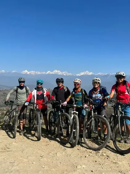 A group of riders posing for a photo with the stunning snow-capped peaks of the Nepal Himalayas behind them. This is what world-class mountain biking looks like.