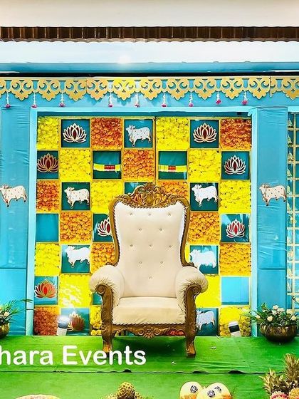 A vibrant Seemantham stage with a blue and yellow color scheme. The checkerboard backdrop is decorated with cow and lotus motifs, creating a cheerful and traditional atmosphere.