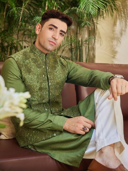 A relaxed portrait showcasing the detailed embroidery of the olive green jacket. The tonal threadwork adds depth and character to the ensemble.