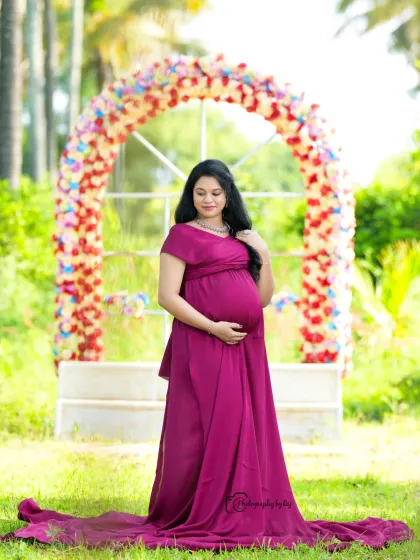 A solo portrait in a wine-colored gown, framed by a floral arch. The natural light and serene expression make this a timeless maternity photo.