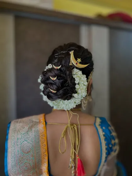 The back view of the hairstyle, showing the neat bun decorated with jasmine and moon-shaped hairpins, a classic choice for Maharashtrian brides.