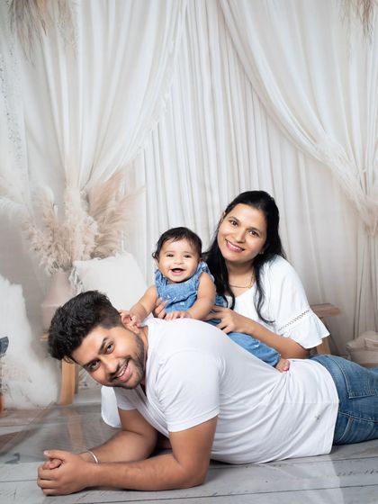 A playful family moment on the floor, with the baby girl climbing on her dad's back while mom looks on.