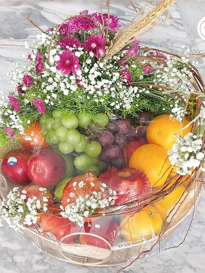 A vibrant and healthy fruit hamper, filled with fresh grapes, apples, and pomegranates, and decorated with pink chrysanthemums.