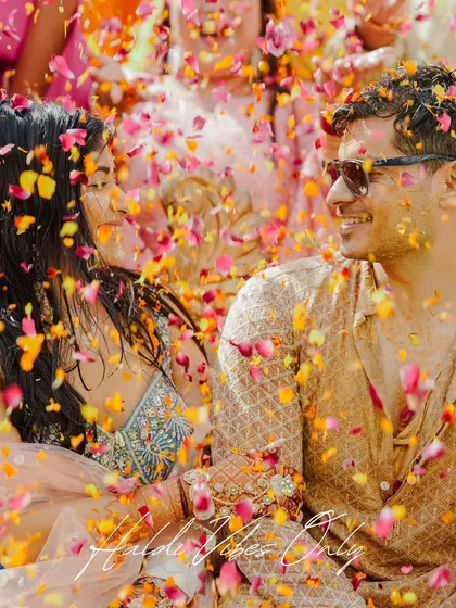 A close-up of the couple amidst a shower of colorful petals. The joy in their eyes is infectious, a perfect memory from their vibrant Haldi function.