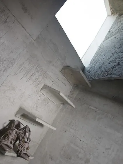 Cantilevered concrete shelves emerge from the wall, serving as minimalist pedestals for displaying accessories. The overhead skylight casts natural light down the textured concrete, highlighting the interplay of form and material.