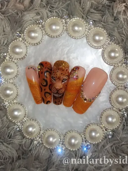 A full set inspired by the leopard, featuring a 3D portrait nail, leopard print, and sparkling orange glitter nails with crystal accents.