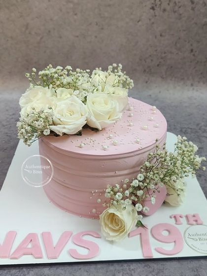 A lovely pink cake adorned with a bouquet of fresh white roses and baby's breath. The simple, clean design makes the flowers the star of the show.