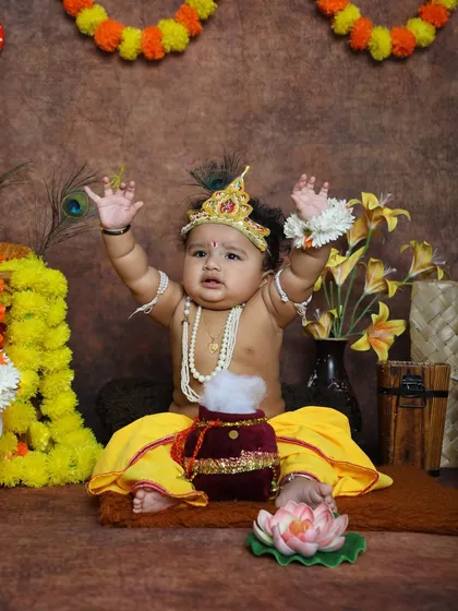 This little Krishna is raising his hands in a playful pose, surrounded by festive decor. We encourage natural expressions to capture the true spirit of your child.