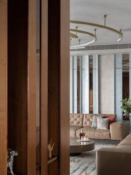 A glimpse into the living room through a wooden partition, revealing the layered textures and tones of the space. This view highlights the mix of leather, fabric, and reflective surfaces that add depth and character to the interior design.
