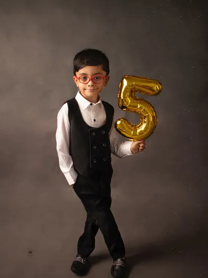 Five and fabulous! This young man is celebrating his fifth birthday in style, holding a golden '5' balloon against a classic charcoal backdrop.