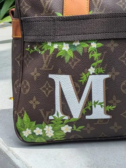 A detailed look at the custom monogram. The clean, sharp edges of the letter contrast with the organic flow of the hand-painted leaves and flowers.