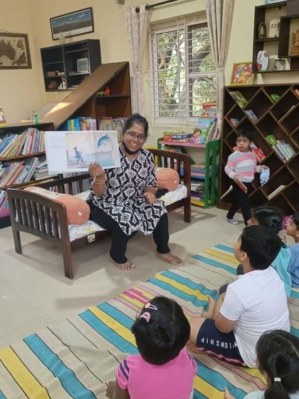 The storyteller holds up the book, showing a beautiful illustration of a dolphin leaping from the water.