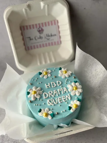 Bento cakes are great for fun and quirky messages. This one, reading "HBD Drama Queen" and decorated with little daisies, is a playful way to celebrate a friend's birthday.