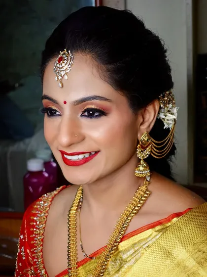 A classic South Indian bridal look with a bright red lip, winged eyeliner, and traditional gold jewellery. Her smile shows her confidence and happiness.
