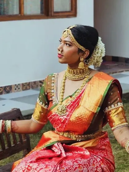 Our elegant bride Pooja, seated in a moment of quiet reflection. She is wearing a full temple jewellery set, including a choker, haram, and vaddanam, that exudes traditional charm.