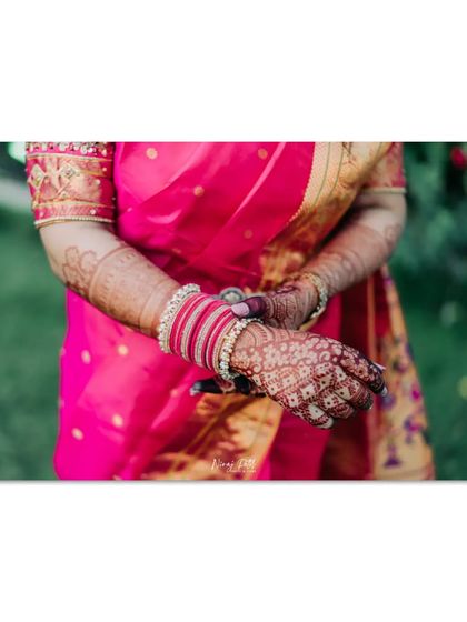 A close-up of the bride's hands, showing how the rich henna stain complements her bright pink saree and bangles.