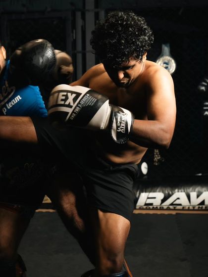 A fighter lands a knee strike during a sparring session, with the coach absorbing the impact.