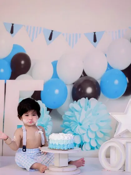 A classic first birthday cake smash. This little boy, dressed in suspenders, is enjoying his blue and white themed cake.
