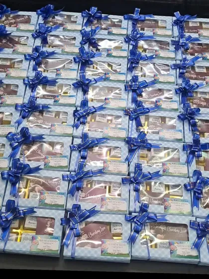 A large order of budget-friendly chocolate boxes going out for a Cocomelon themed first birthday. The blue checkered boxes are filled with six chocolates and tied with a matching ribbon.