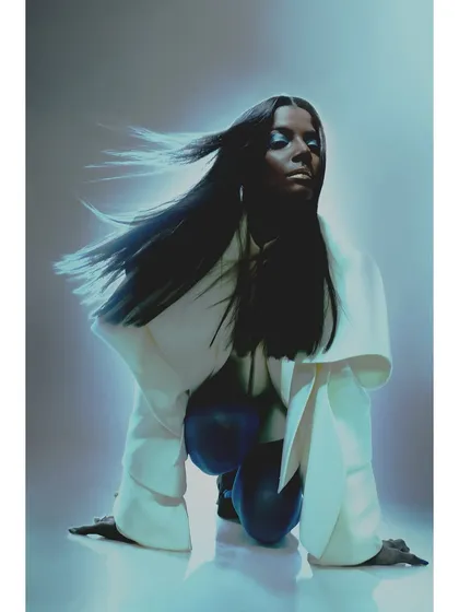A powerful, low-angle shot. The model is styled in a white architectural coat, and the blue lighting from below creates a heroic, otherworldly mood.