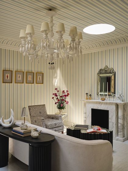 A closer view of the salon, showing the contrast between the curved ivory sofa and a patterned bergère chair. The space is designed to feel composed yet curious, with a restored marble fireplace as its anchor.
