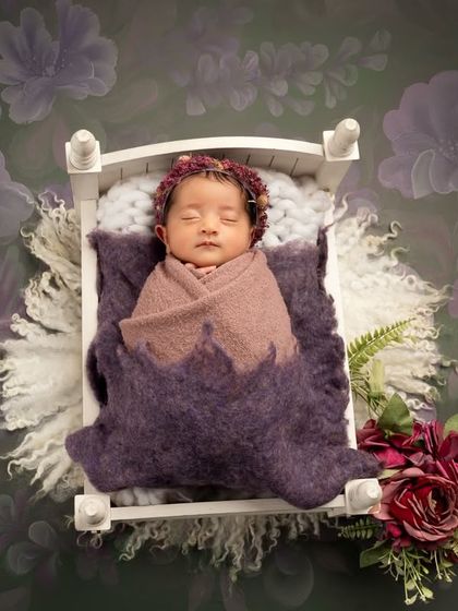 Another variation of the baby-in-a-cot pose. This wider shot includes a floral background and a small bouquet, creating a complete and beautifully styled scene.