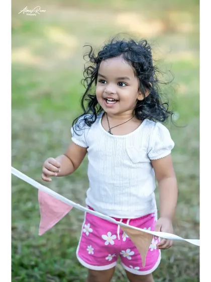A joyful, candid shot of Riona playing with a string of bunting flags. Her bright smile and the natural outdoor lighting make this a perfect example of a spontaneous moment captured forever.
