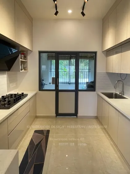 A spacious parallel kitchen with handle-less cabinets in a light beige glossy finish. The layout provides ample counter space and storage, making it highly functional for everyday cooking.