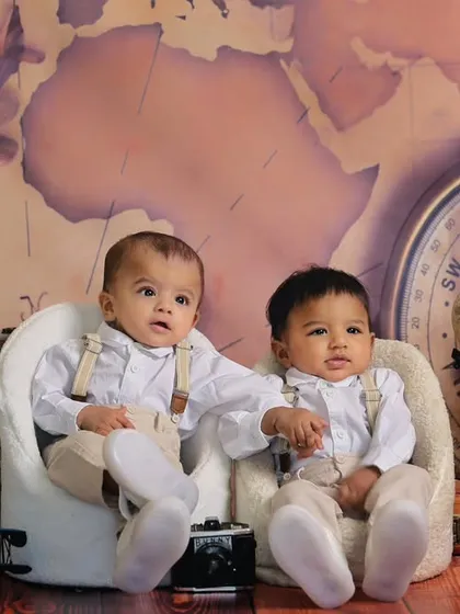 A vintage travel-themed photoshoot for six-month-old twins. Dressed in classic outfits with suspenders, they are ready for an adventure with globes and suitcases as props.