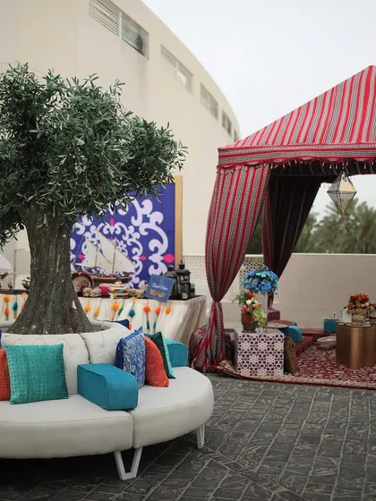 A chic lounge area at the Bahrain wedding, with a circular sofa, an olive tree centerpiece, and views of the Moroccan tents, blending modern comfort with the event's theme.