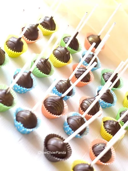 A large batch of classic chocolate cake pops, each placed in a colourful paper liner. These are a simple and delicious option for kids' parties or large gatherings.