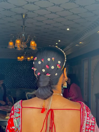 The final look of the sleek low bun with scattered flowers, a perfect hairstyle for a modern bride wearing a matha patti and other traditional jewelry.